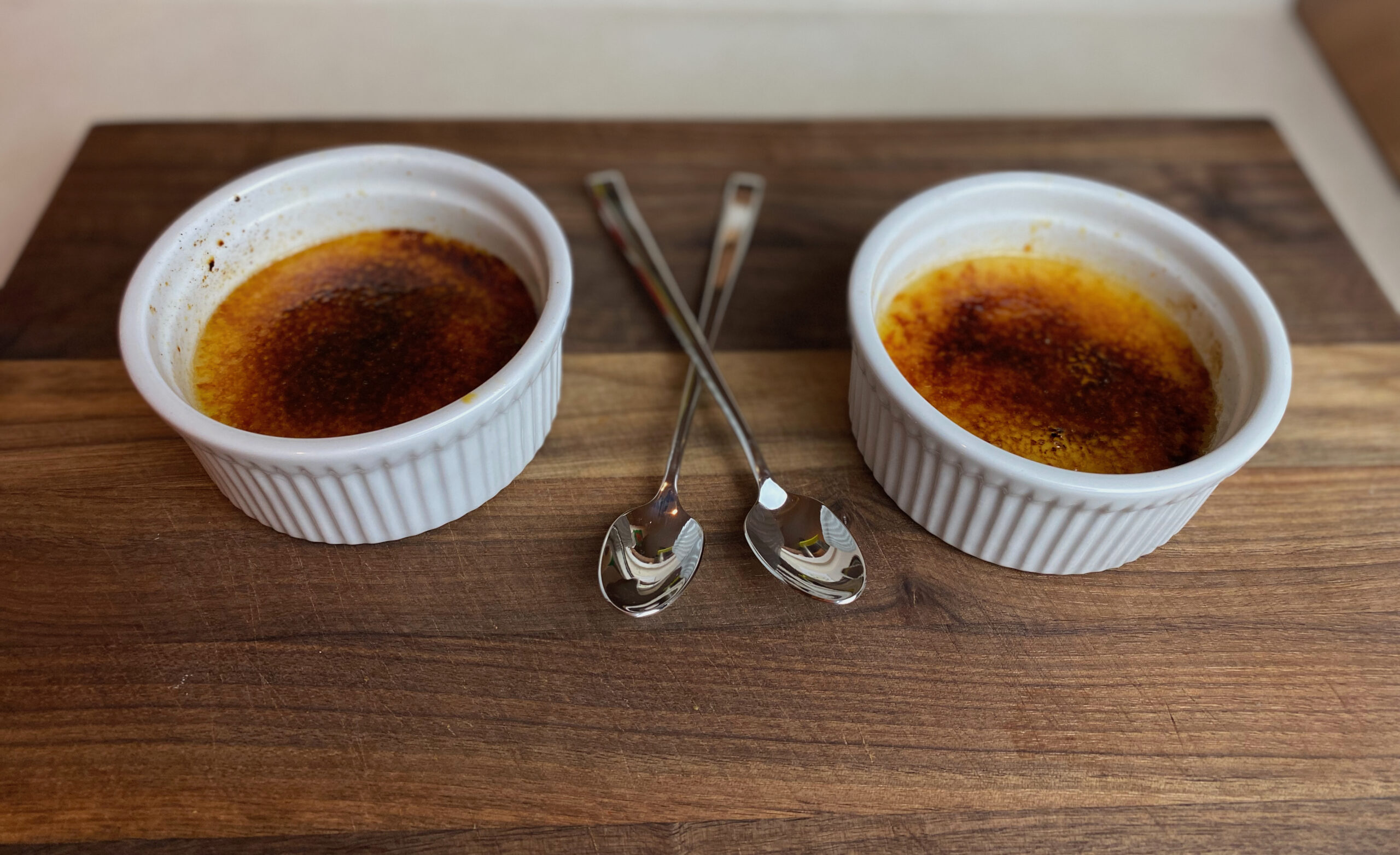 two ramekins with creme brulee inside and two spoons