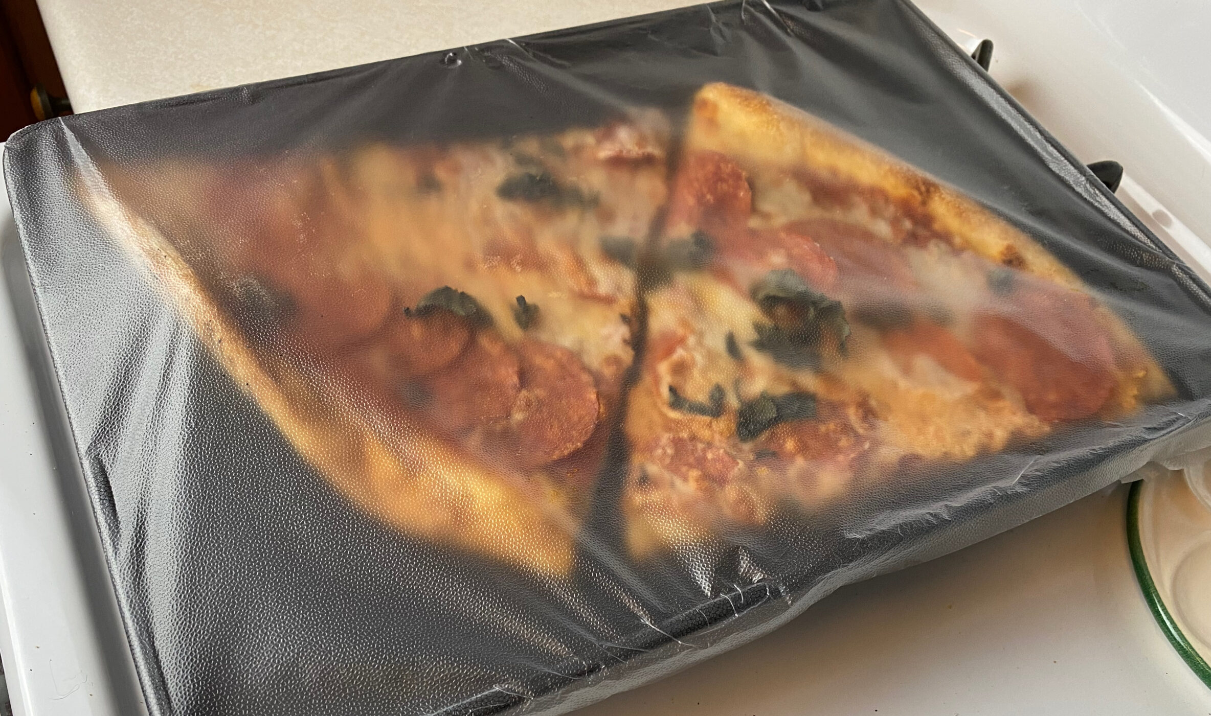 two slices of pizza on a baking pan covered by cling wrap
