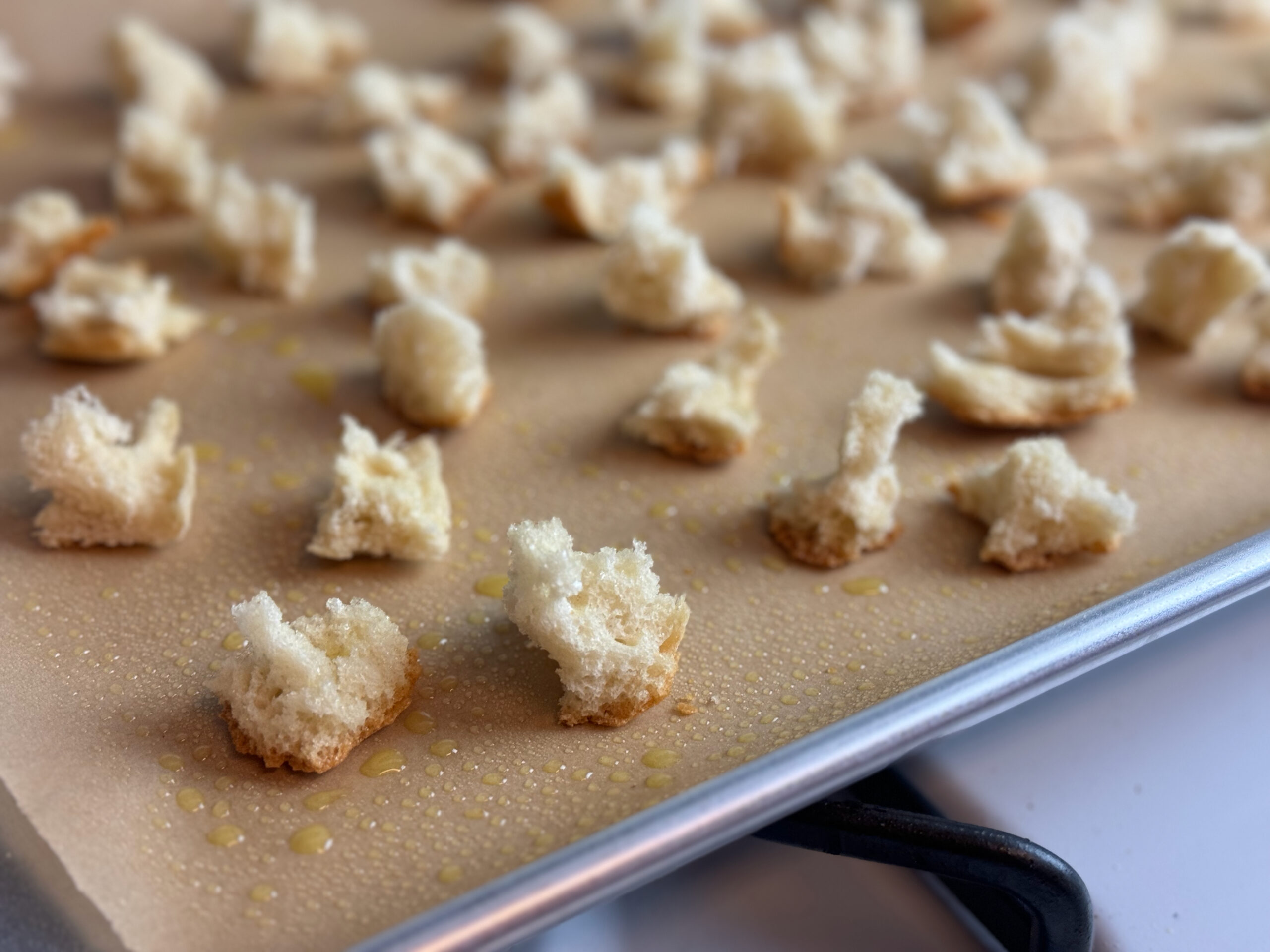 bread spritzed with olive oil as a step to making homemade croutons