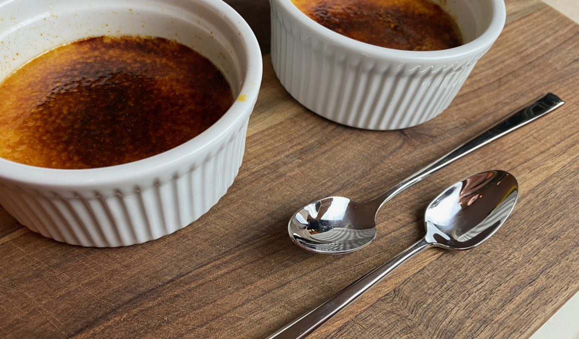 two ramekins with creme brulee and two spoons